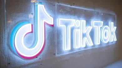 Illuminated TikTok logo sign with neon-style lighting on a textured wall.