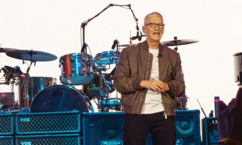 Tim Cook stands on stage in front of a drum set and amplifiers.