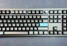 Gray mechanical keyboard with blue accent keys on a dark gray surface.