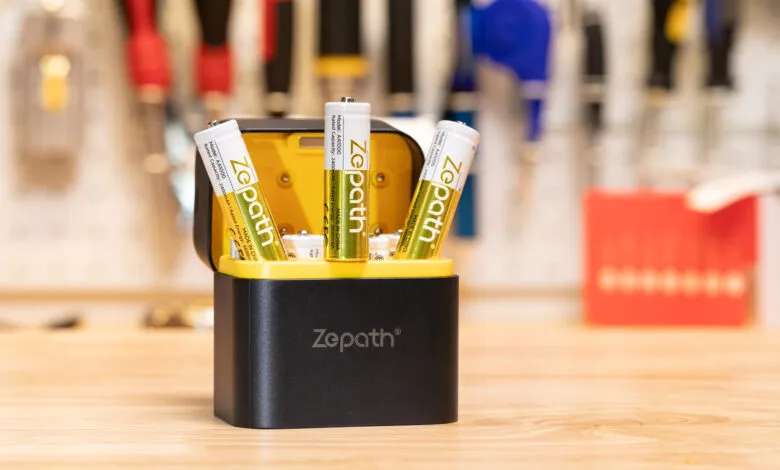Three ZePath AA batteries in a black and yellow charger on a wooden surface.
