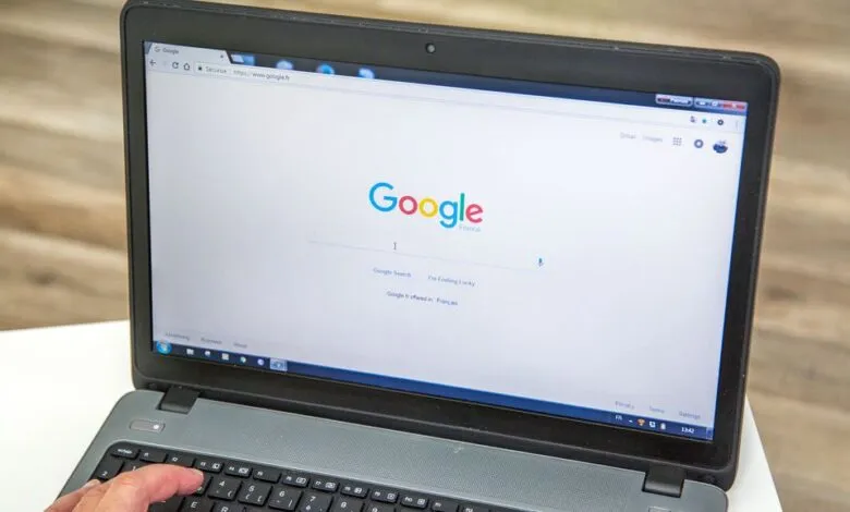 Laptop displaying Google search engine with a hand on the keyboard.