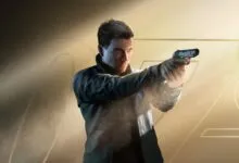 Man in black jacket aiming a pistol against a golden background.