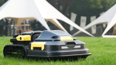 Black and yellow Yarbo robot lawnmower on green grass.