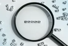Magnifying glass focuses on 'BRAND' spelled with letter beads.