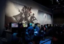 Gamers play Destiny 2 at a gaming convention, large backdrop.