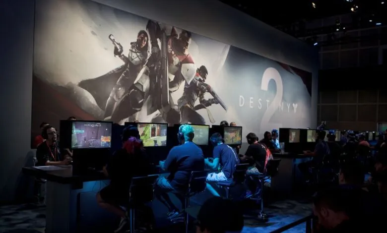 Gamers play Destiny 2 at a gaming convention, large backdrop.
