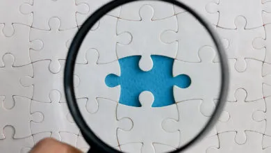 Magnifying glass over white puzzle with one piece missing, revealing blue.