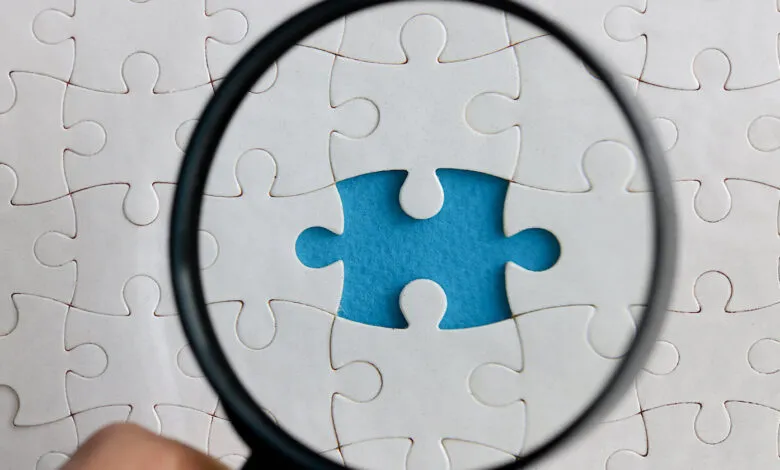 Magnifying glass over white puzzle with one piece missing, revealing blue.