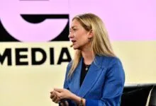 Woman with blonde hair speaks at a media event, wearing a blue blazer.