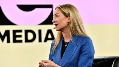 Woman with blonde hair speaks at a media event, wearing a blue blazer.