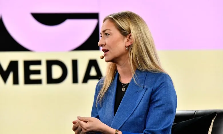 Woman with blonde hair speaks at a media event, wearing a blue blazer.