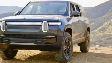 Rivian R1S electric SUV parked on a dirt road with mountains in the background.