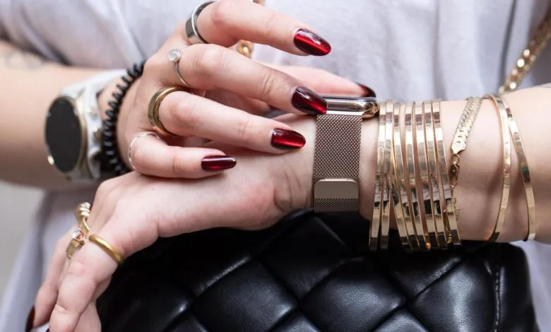 Woman's hands with Apple Watch, bracelets, and rings on a quilted bag.