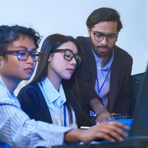 Three young professionals collaborate on a computer, focusing on the screen.