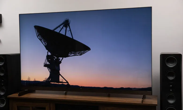 Large TV displays a silhouetted radio telescope against a colorful sunset sky.