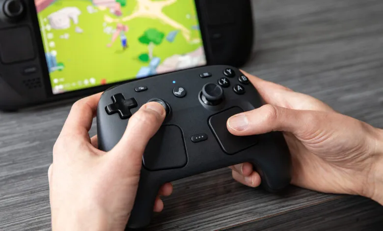 Hands hold a Steam Controller in front of a Steam Deck, playing a game.