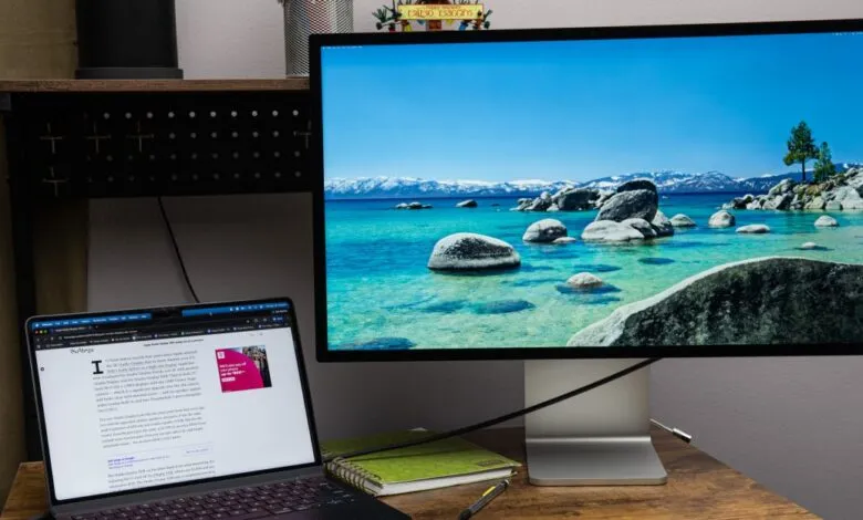 Laptop and large monitor displaying a scenic lake view on a wooden desk.
