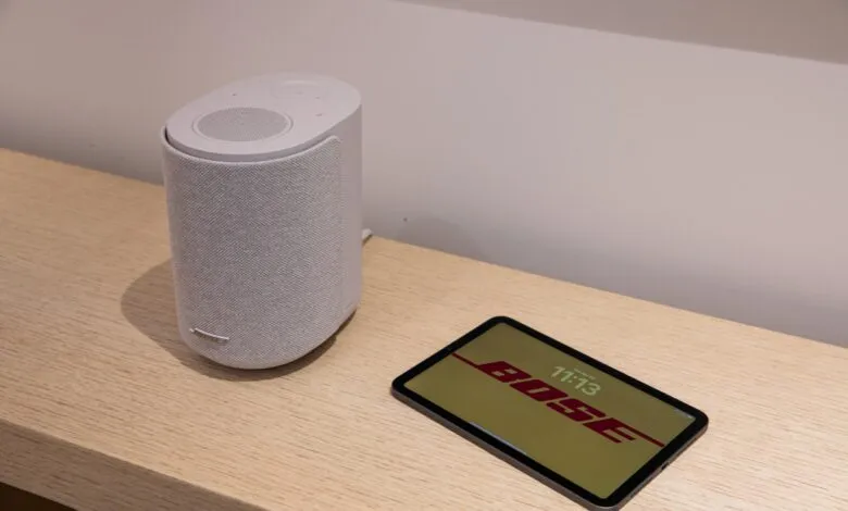 Bose speaker and tablet displaying Bose logo on a wooden surface.