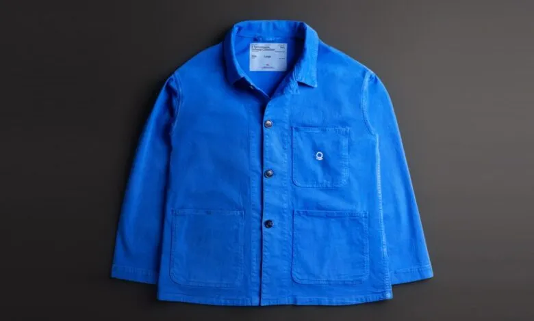 Bright blue chore coat with pockets and logo on a dark gray background.