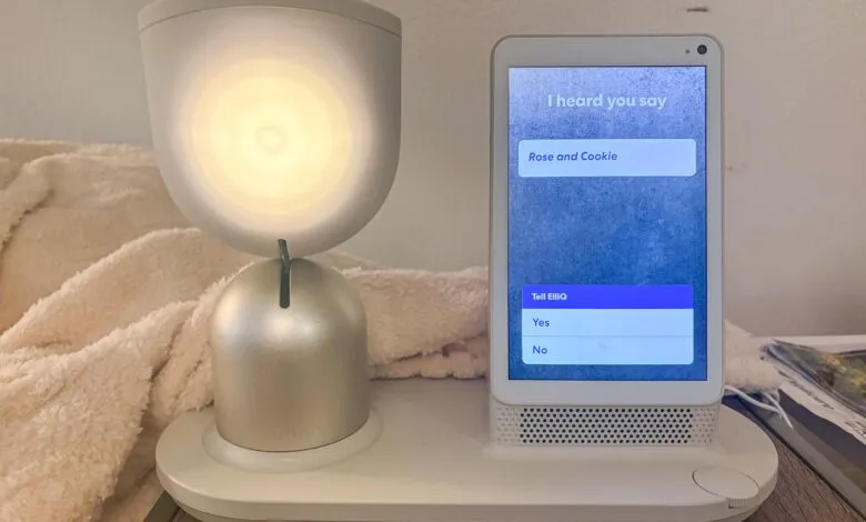 ElliQ robot on a table, screen displays 'Rose and Cookie' and 'Tell ElliQ'