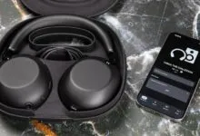 Black Sony 1000X headphones in case next to phone displaying app.