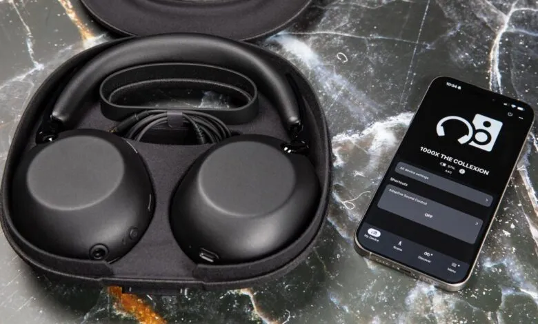 Black Sony 1000X headphones in case next to phone displaying app.