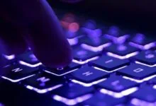 Close-up of a finger pressing a key on a backlit purple gaming keyboard.