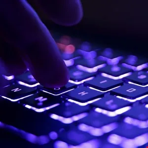 Close-up of a finger pressing a key on a backlit purple gaming keyboard.