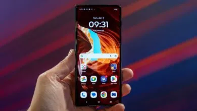 Hand holding a Motorola smartphone displaying its home screen.