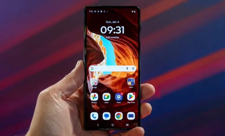 Hand holding a Motorola smartphone displaying its home screen.