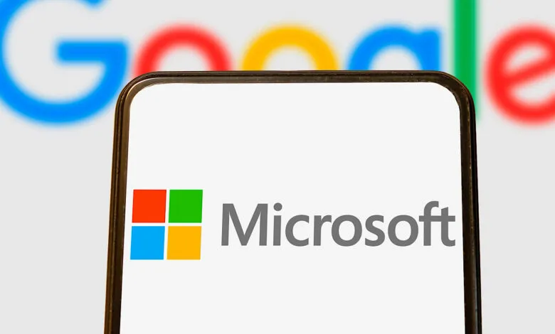 Microsoft logo on phone screen with blurred Google logo in background.