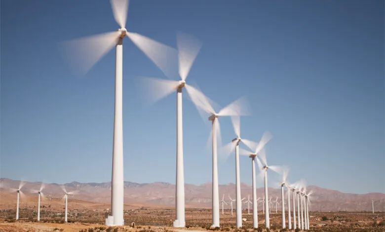 Row of wind turbines spinning in a desert landscape under a clear blue sky.
