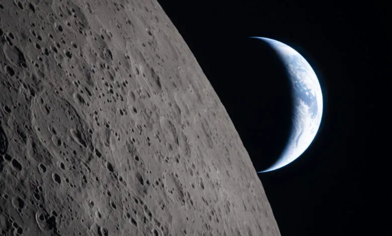 Crescent Earth rising over the lunar horizon, craters visible.