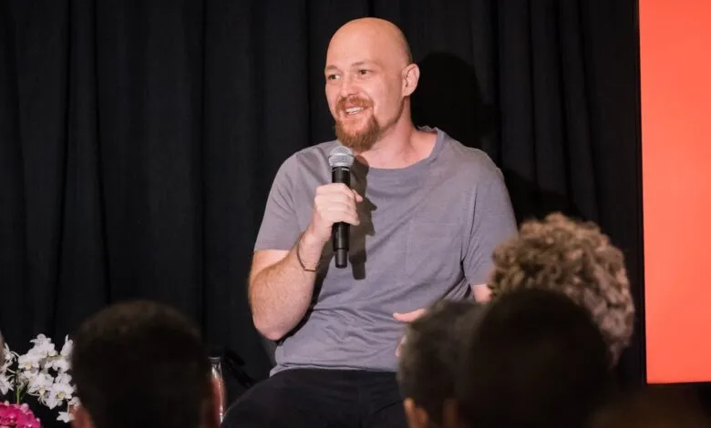 Bald man with beard speaking into microphone on stage.