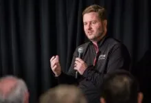 Man speaks into microphone at event, gesturing with hand.