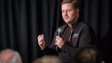 Man speaks into microphone at event, gesturing with hand.