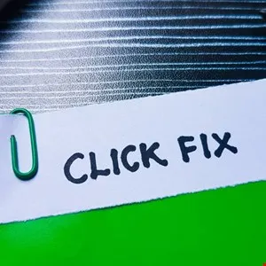 White paper with 'CLICK FIX' text, secured with a green paperclip, on a textured surface.