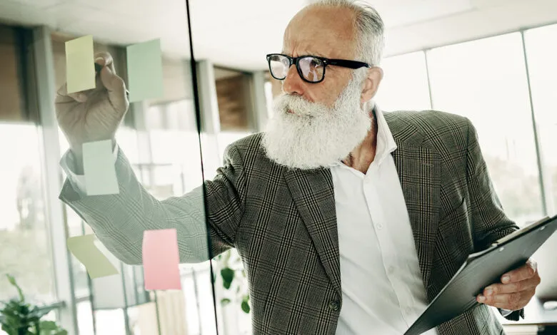 Senior businessman with beard planning on glass board with sticky notes.