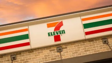 7-Eleven store sign with orange, green, and red stripes against a sunset sky.