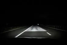 Nighttime view of a highway illuminated by car headlights.