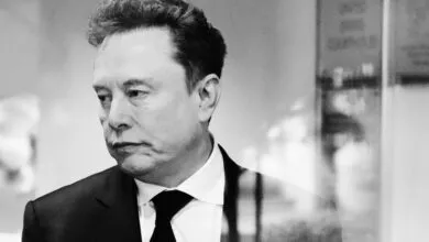 Black and white portrait of Elon Musk in a suit and tie.