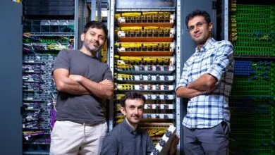 Three men stand in front of server racks, arms crossed, smiling slightly.