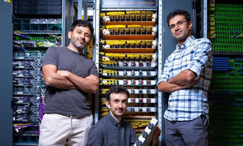 Three men stand in front of server racks, arms crossed, smiling slightly.