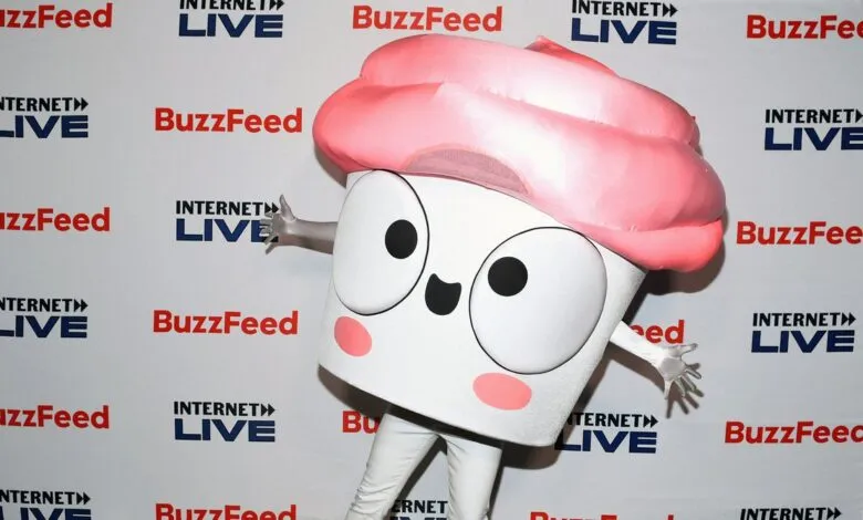 Cupcake mascot poses in front of BuzzFeed Internet Live backdrop.