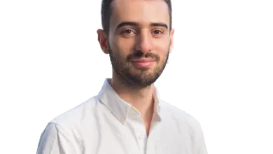 Portrait of a man with a beard wearing a white shirt against a black background.