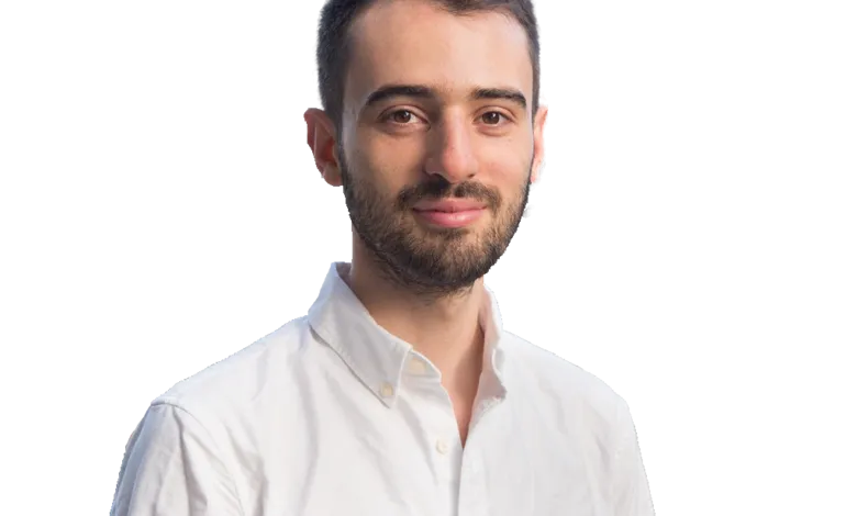 Portrait of a man with a beard wearing a white shirt against a black background.