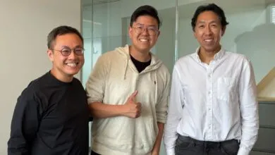 Three smiling men pose indoors against a neutral background.