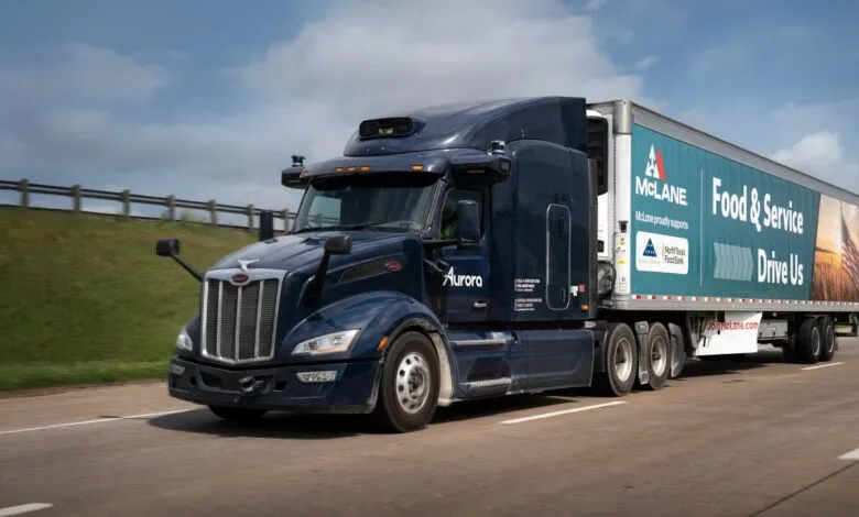 Autonomous McLane semi-truck driving on highway, Aurora logo visible.