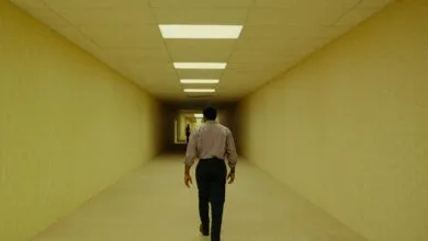 Man walks down a long, yellow hallway with fluorescent lights.