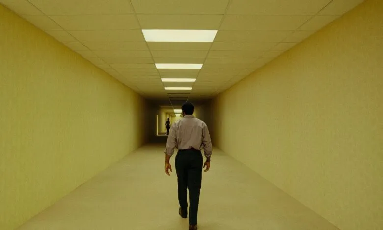 Man walks down a long, yellow hallway with fluorescent lights.